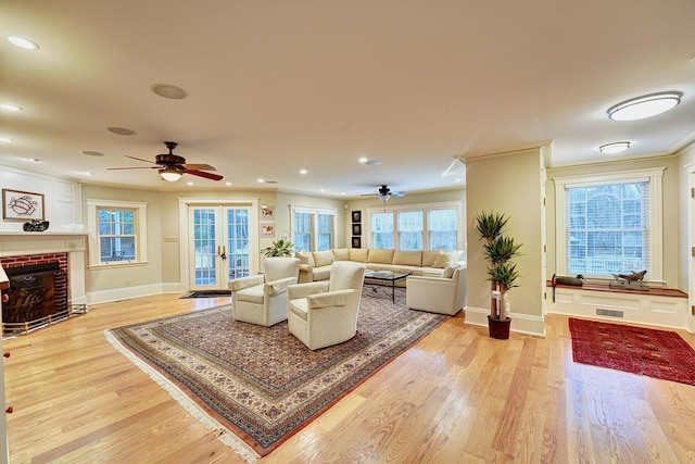 living room featuring french doors, ceiling fan, ornamental molding, a fireplace, and light hardwood / wood-style floors