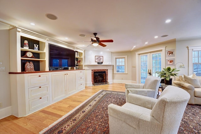 living room with ceiling fan, french doors, a brick fireplace, light hardwood / wood-style floors, and ornamental molding