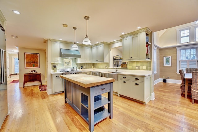 kitchen with light wood-type flooring, tasteful backsplash, wall chimney exhaust hood, pendant lighting, and a kitchen island