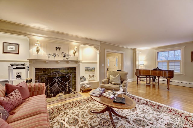 living room with baseboard heating, a tiled fireplace, wood-type flooring, and ornamental molding