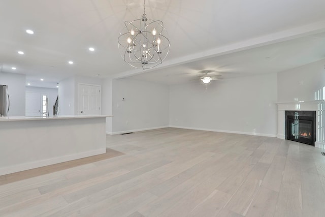 unfurnished living room with a fireplace, ceiling fan with notable chandelier, and light hardwood / wood-style flooring