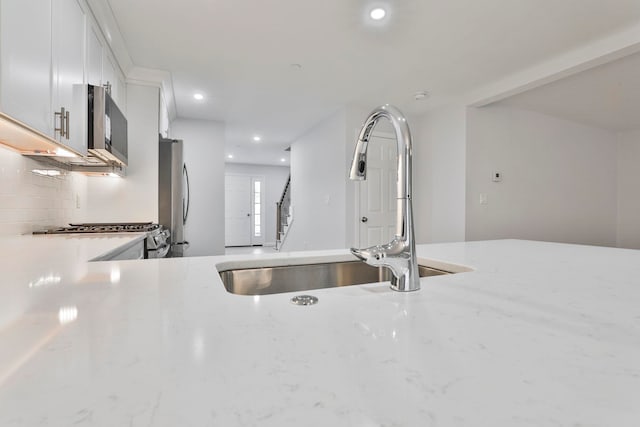 kitchen with stainless steel fridge, light stone counters, white cabinetry, and sink