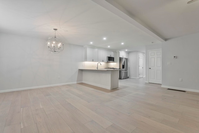 kitchen with kitchen peninsula, stainless steel appliances, pendant lighting, beamed ceiling, and white cabinetry