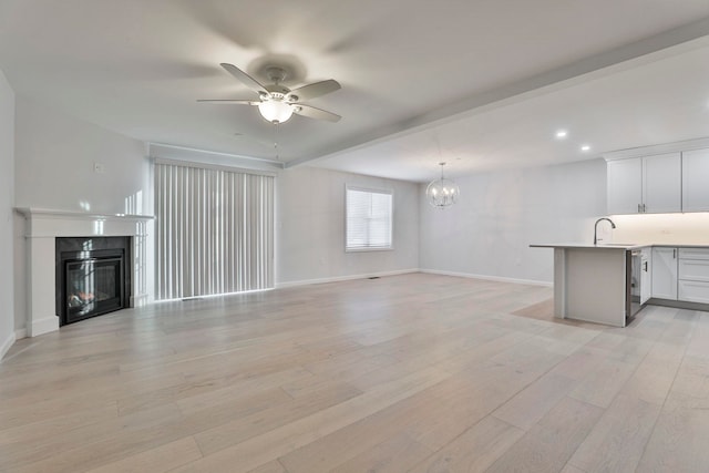 unfurnished living room featuring light wood-type flooring, ceiling fan with notable chandelier, and sink