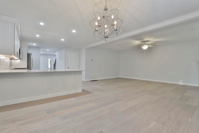 unfurnished living room featuring ceiling fan with notable chandelier and light hardwood / wood-style floors