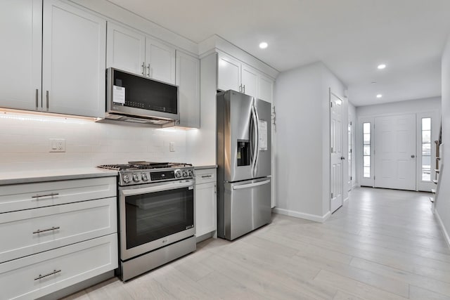 kitchen featuring tasteful backsplash, white cabinets, light wood-type flooring, and appliances with stainless steel finishes