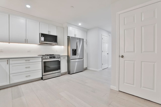 kitchen with white cabinets, appliances with stainless steel finishes, decorative backsplash, and light hardwood / wood-style floors