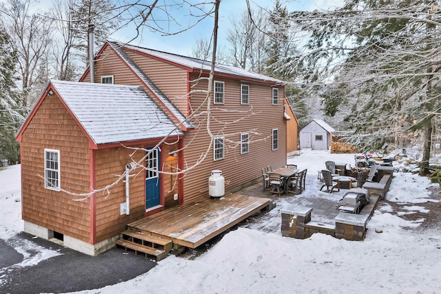 snow covered back of property with a shed and a deck