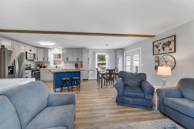 living room featuring beam ceiling, light hardwood / wood-style flooring, french doors, and sink