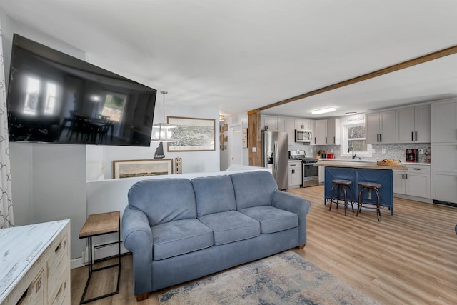 living room with light wood-type flooring, a baseboard heating unit, and sink