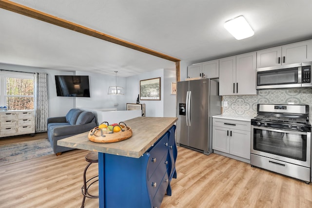 kitchen featuring blue cabinets, a kitchen island, a kitchen bar, butcher block counters, and stainless steel appliances