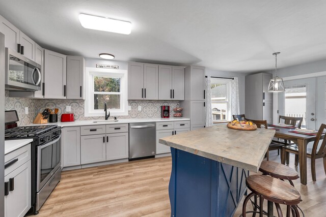 kitchen with appliances with stainless steel finishes, a kitchen breakfast bar, tasteful backsplash, sink, and decorative light fixtures