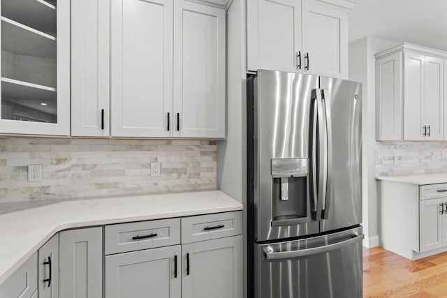 kitchen with tasteful backsplash, light stone countertops, stainless steel refrigerator with ice dispenser, and light hardwood / wood-style flooring