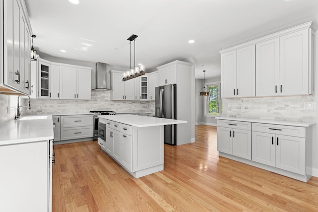 kitchen with a center island, wall chimney range hood, sink, appliances with stainless steel finishes, and white cabinetry