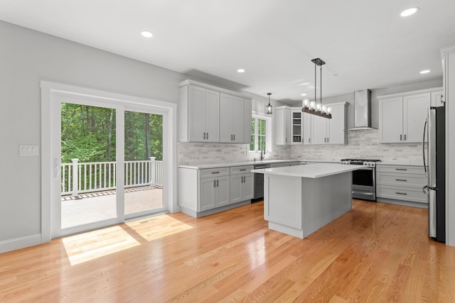 kitchen featuring a wealth of natural light, hanging light fixtures, stainless steel appliances, wall chimney range hood, and a kitchen island