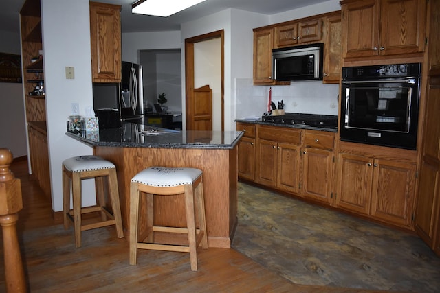 kitchen with stainless steel fridge, gas cooktop, black oven, dark stone countertops, and a breakfast bar