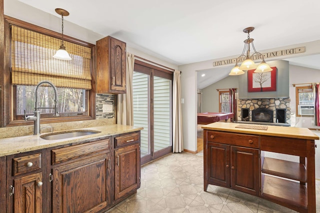 kitchen with pendant lighting, lofted ceiling, sink, light stone countertops, and tasteful backsplash