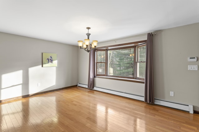 spare room featuring light wood-type flooring, baseboard heating, and a notable chandelier