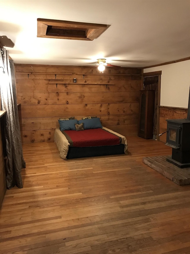 bedroom with a wood stove, wooden walls, ceiling fan, and wood-type flooring