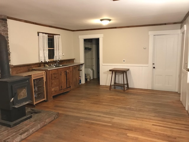 bar featuring a wood stove, sink, light wood-type flooring, and ornamental molding