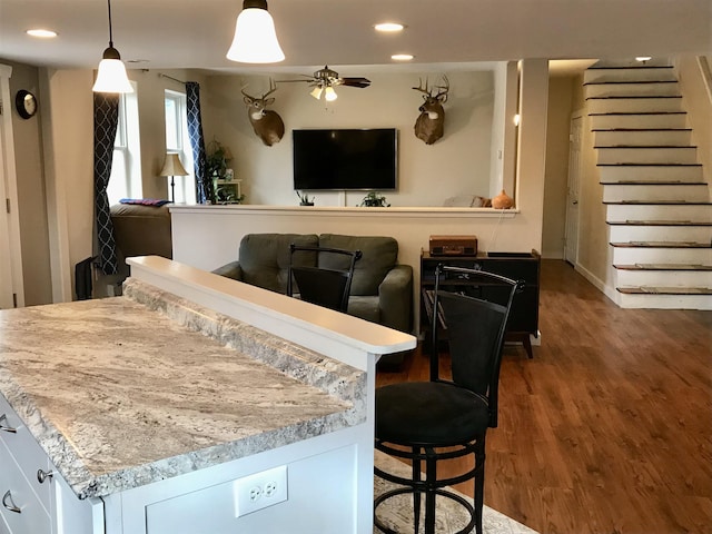 interior space with a kitchen breakfast bar, ceiling fan, pendant lighting, white cabinetry, and dark hardwood / wood-style floors