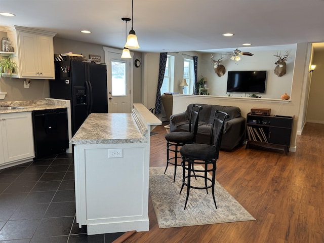 kitchen with white cabinetry, hanging light fixtures, a center island, black appliances, and a kitchen bar