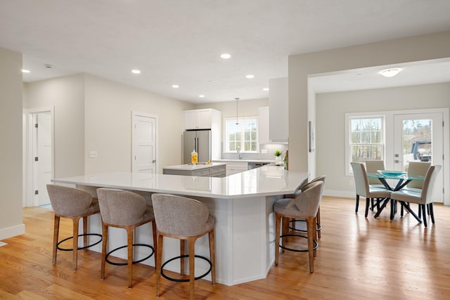 kitchen featuring pendant lighting, white cabinets, light hardwood / wood-style flooring, high quality fridge, and kitchen peninsula