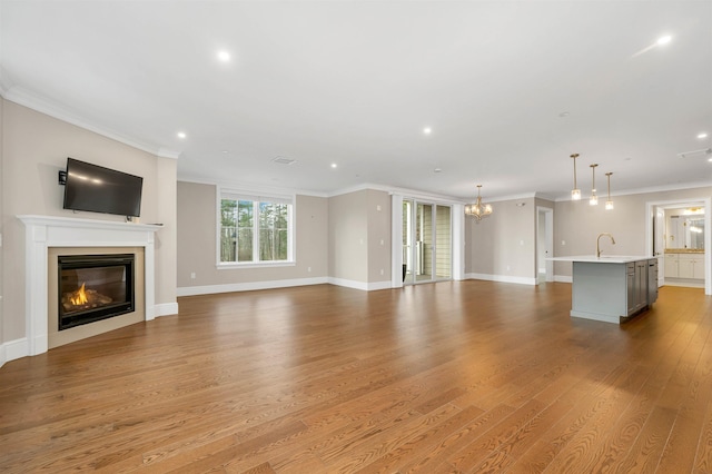 unfurnished living room with wood-type flooring, an inviting chandelier, ornamental molding, and sink