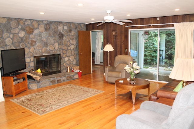 living room with hardwood / wood-style flooring, ceiling fan, wood walls, and a fireplace