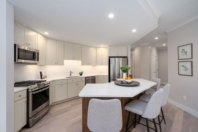 kitchen with stainless steel appliances, sink, white cabinets, a center island, and light hardwood / wood-style floors