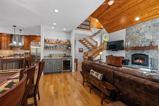 living room with a stone fireplace, vaulted ceiling, light wood-type flooring, wood ceiling, and beverage cooler