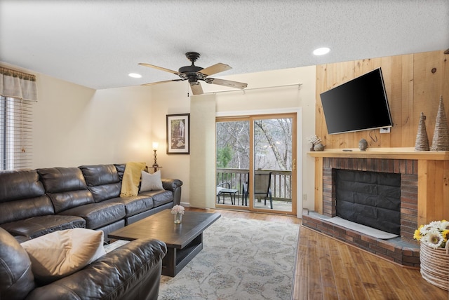 living room featuring a textured ceiling, ceiling fan, wood-type flooring, a fireplace, and wood walls