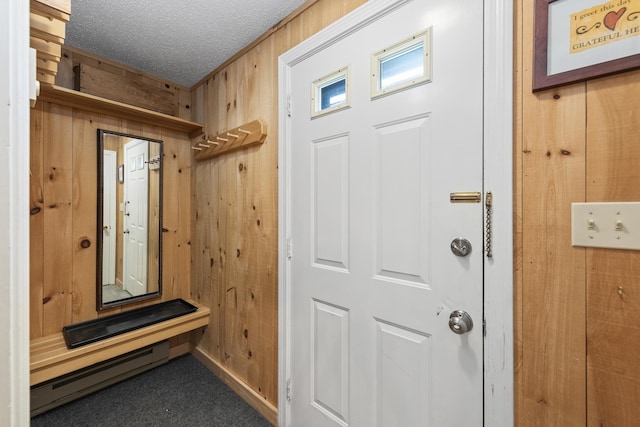 mudroom featuring wooden walls, a baseboard radiator, dark carpet, and a textured ceiling