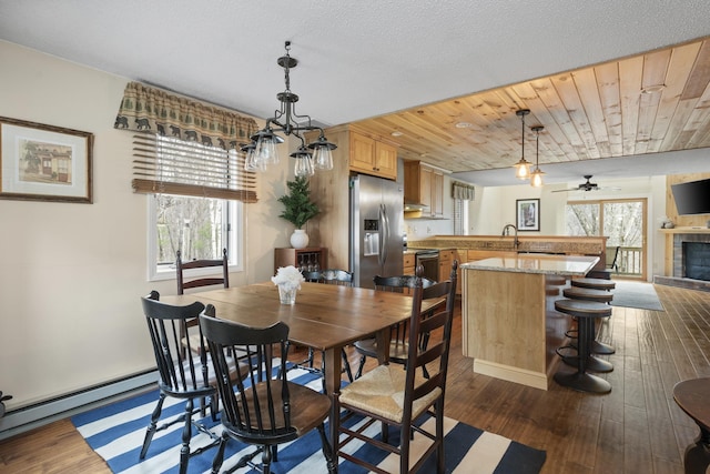 dining area featuring baseboard heating, dark wood-type flooring, ceiling fan, wooden ceiling, and a tiled fireplace