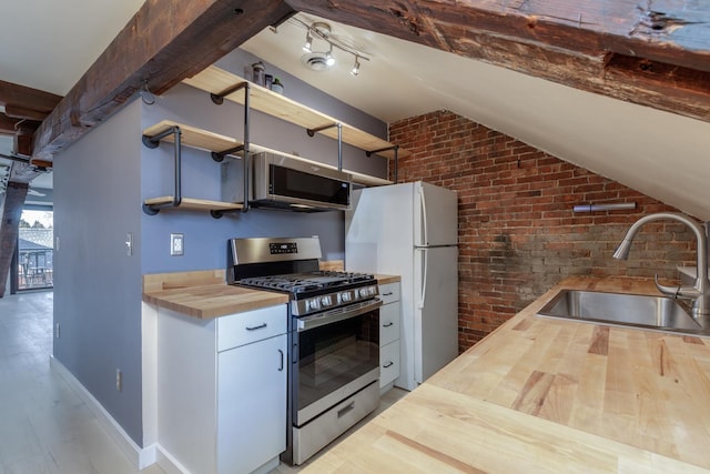 kitchen featuring appliances with stainless steel finishes, light wood-type flooring, brick wall, butcher block countertops, and sink