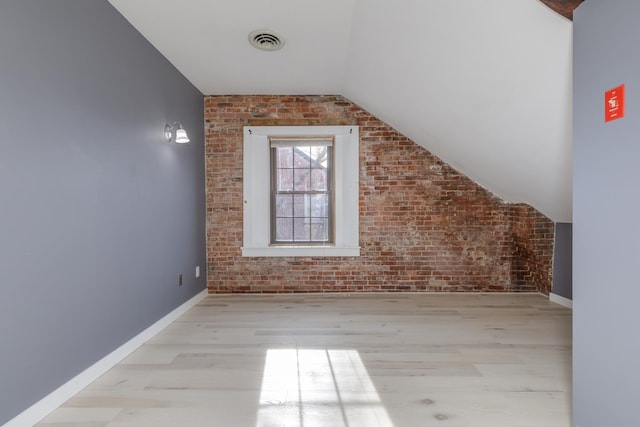 additional living space with brick wall, vaulted ceiling, and light hardwood / wood-style floors