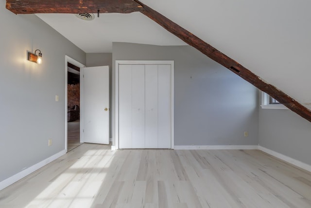 additional living space with light hardwood / wood-style floors and beam ceiling