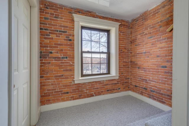 unfurnished room with a textured ceiling, carpet floors, and brick wall