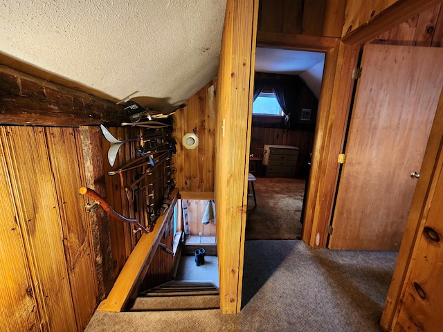 interior space featuring a textured ceiling, wooden walls, dark carpet, and lofted ceiling