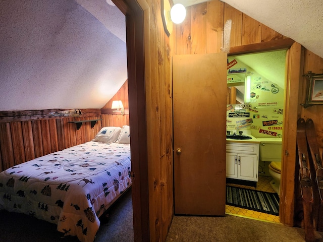 carpeted bedroom with wood walls, sink, lofted ceiling, and a textured ceiling