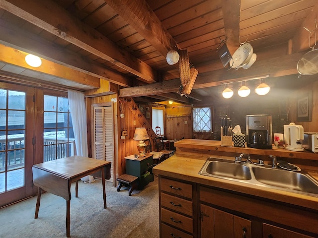 kitchen with beamed ceiling, a wealth of natural light, carpet flooring, and wooden walls