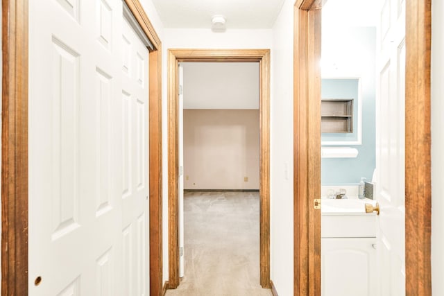 corridor featuring sink, light colored carpet, and a textured ceiling