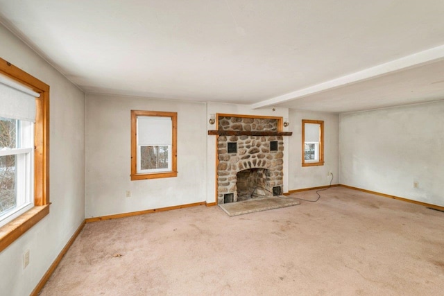 unfurnished living room with beamed ceiling, a stone fireplace, and light colored carpet