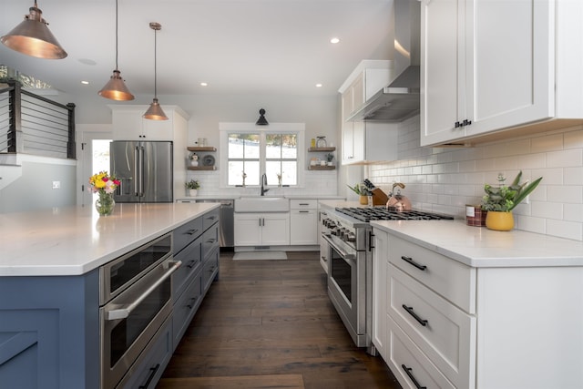 kitchen with pendant lighting, high end appliances, white cabinets, sink, and wall chimney exhaust hood