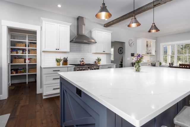 kitchen with wall chimney range hood, beamed ceiling, backsplash, pendant lighting, and white cabinets