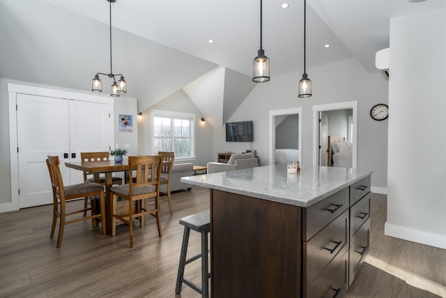 kitchen with pendant lighting, dark wood-type flooring, light stone countertops, dark brown cabinets, and a kitchen island