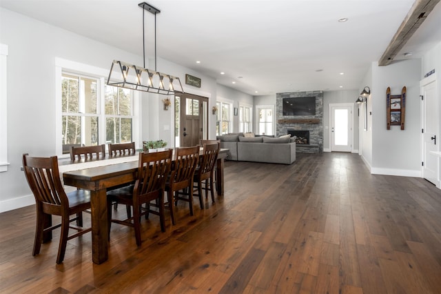 dining area with a stone fireplace and dark wood-type flooring