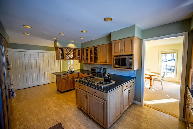 kitchen with decorative backsplash, light colored carpet, kitchen peninsula, and stainless steel appliances