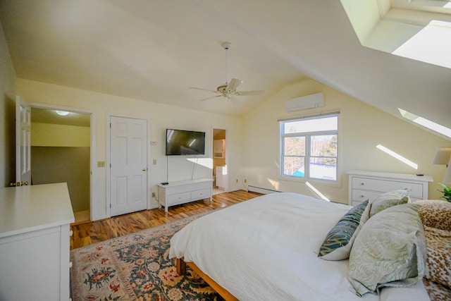 bedroom featuring a wall mounted air conditioner, vaulted ceiling with skylight, baseboard heating, ceiling fan, and light hardwood / wood-style floors