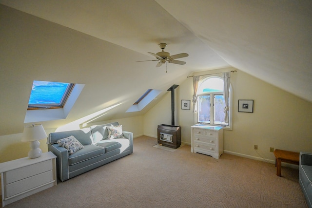 additional living space with a wood stove, ceiling fan, vaulted ceiling with skylight, and light colored carpet